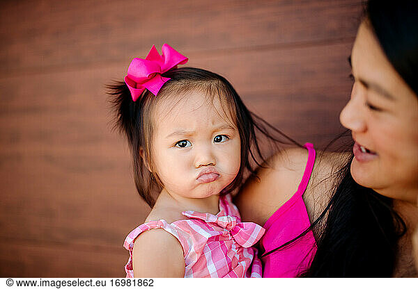 Cute asian toddler with pink bow in hair makes pouty face