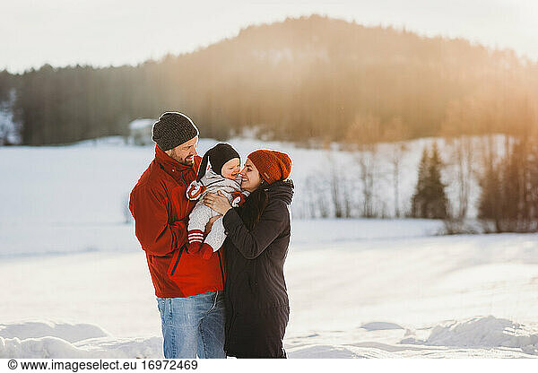 Cute baby and parents in snowy mountains in winter sunny day smiling