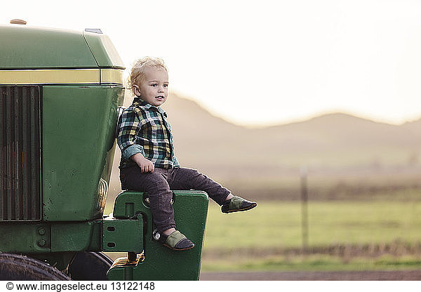 Cute baby boy sitting on tractor against clear sky
