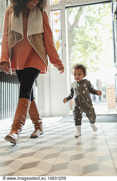 Cute baby daughter following mother in entry corridor