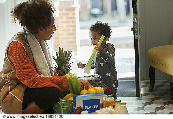Cute baby daughter helping mother unload grocery delivery