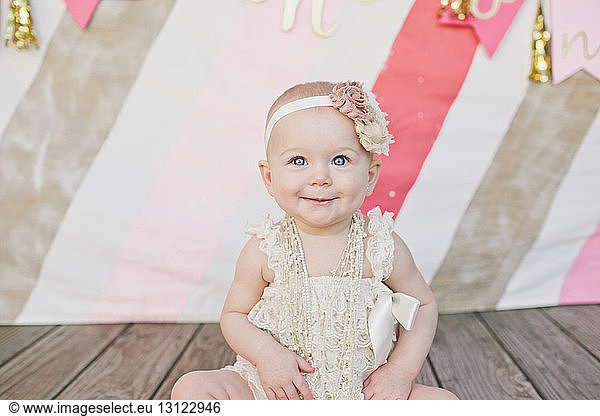 Cute baby girl looking away while sitting on floorboard at birthday party