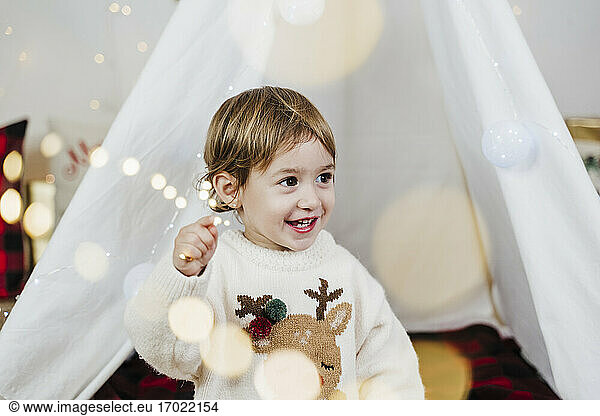 Cute baby girl looking away while standing against tent at home during Christmas