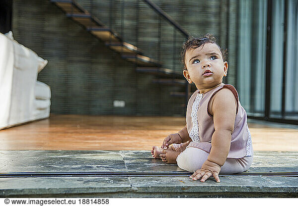 Cute baby girl sitting on floor at home