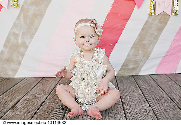 Cute baby girl sitting on floorboard at birthday party