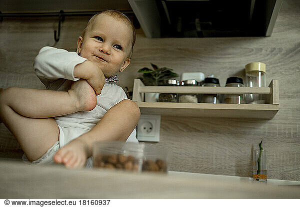 Cute baby girl sitting on kitchen counter at home