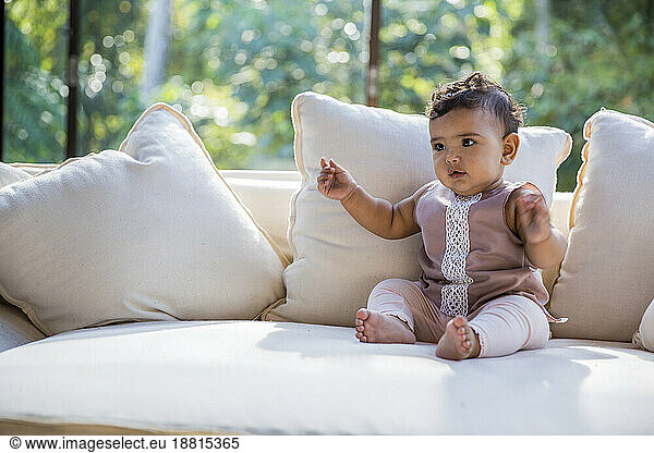 Cute baby girl sitting on sofa at home