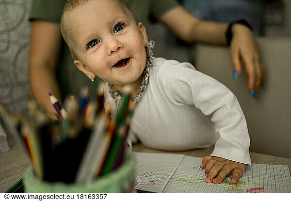 Cute baby girl with drawing book and color pencil at home
