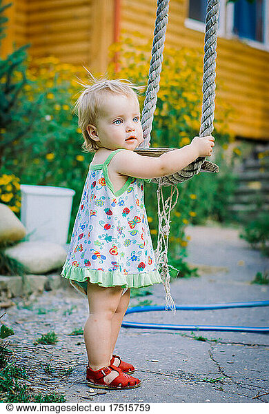 Cute baby girl 3-4 year old in the garden plays a rustic swing