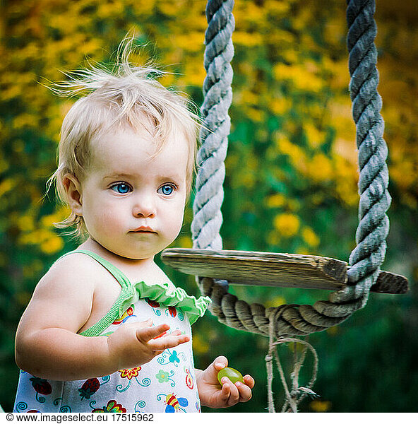 Cute baby girl 3-4 year old in the garden plays a rustic swing