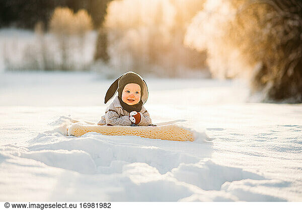 Cute baby smiling sitting on snow during sunset in Norwegian forest