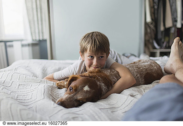 Cute boy cuddling with dog on bed