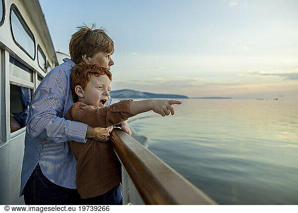 Cute boy gesturing towards sea with grandmother enjoying on ship at dusk