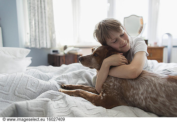 Cute boy hugging dog on bed