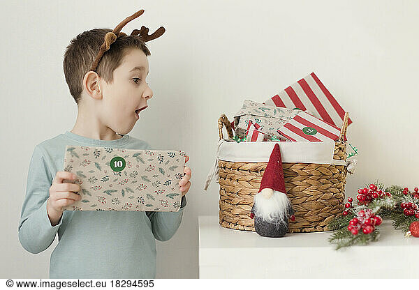 Cute boy looking at Advent gifts in basket by wall