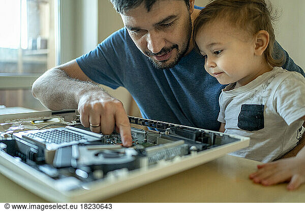 Cute boy looking at father repairing computer on table