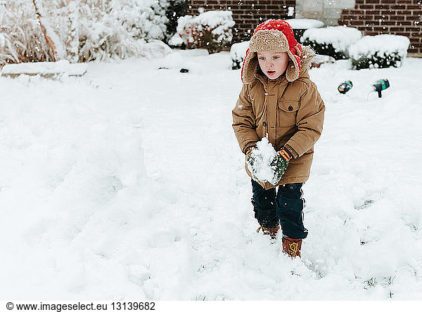 Cute boy looking down while making snowball in yard