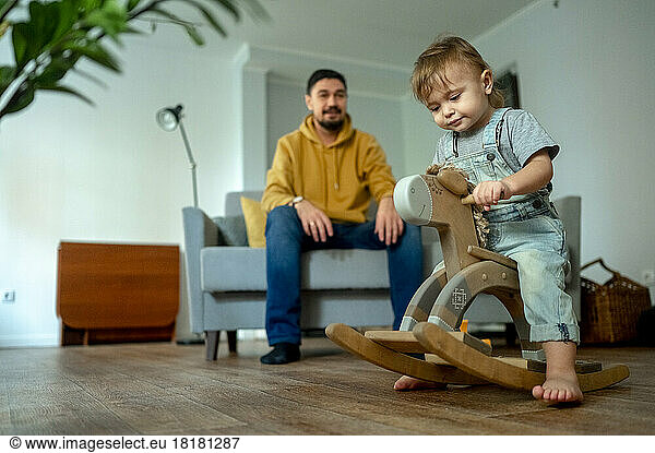 Cute boy playing on rocking horse with father in background