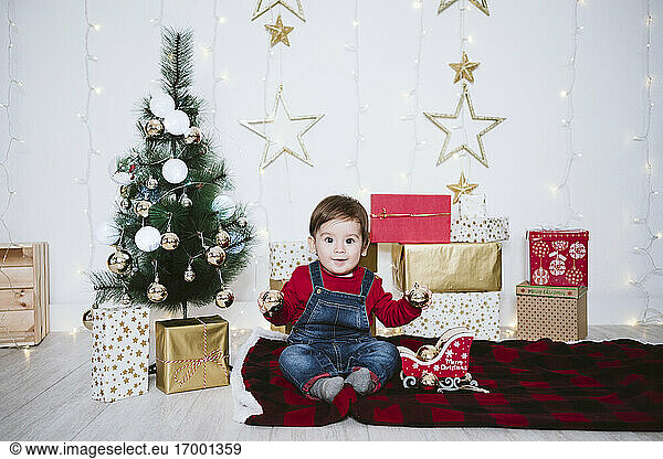 Cute boy playing with bauble while sitting on blanket at home during Christmas