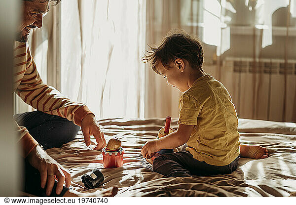 Cute boy playing with father on bed at home