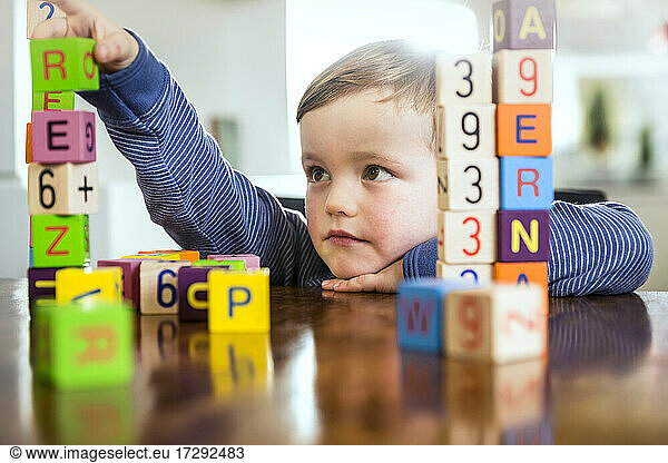 Cute boy playing with toy blocks on table at home