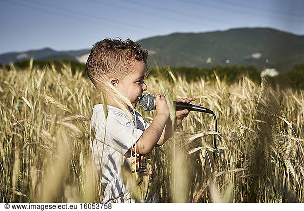 Cute boy singing over microphone while standing amidst crops during sunny day