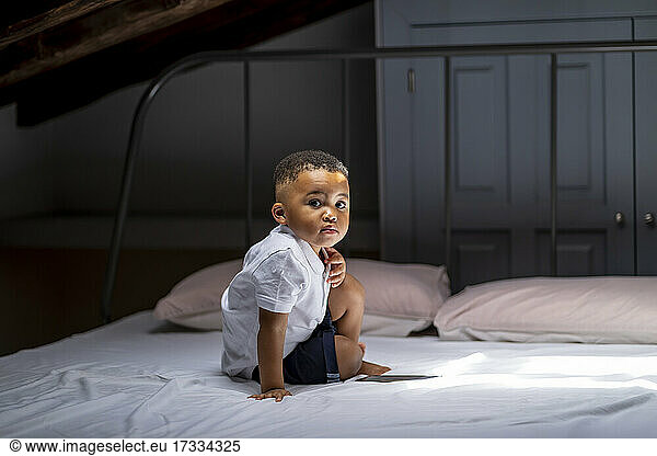 Cute boy sitting on bed in attic at home