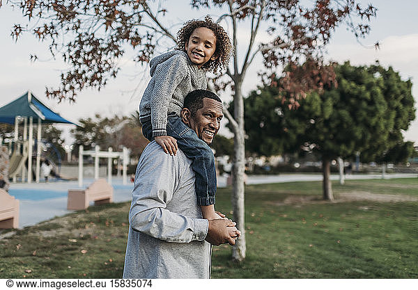 Cute boy sitting on happy father's shoulders at park playground