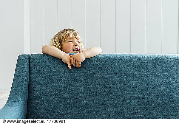 Cute boy standing behind sofa in living room at home