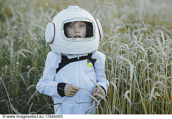 Cute boy wearing space suit and helmet at field