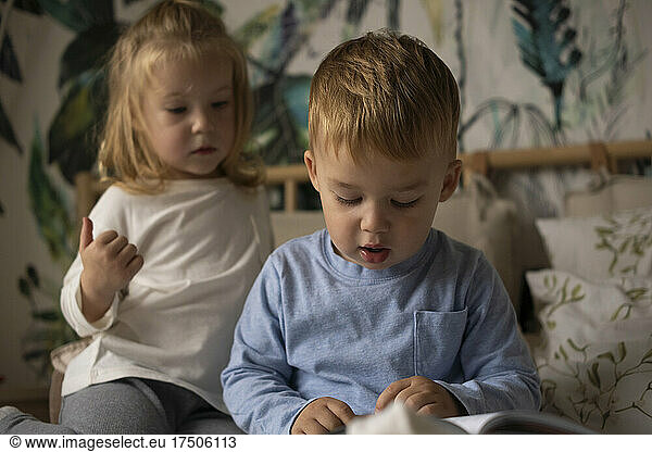 Cute boy with book and twin sister in bedroom at home