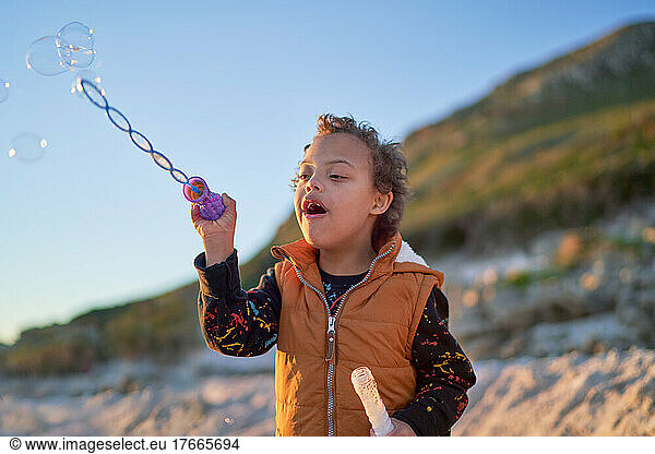 Cute boy with Down Syndrome blowing bubbles on beach