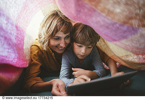 Cute boy with mother using tablet PC under blanket