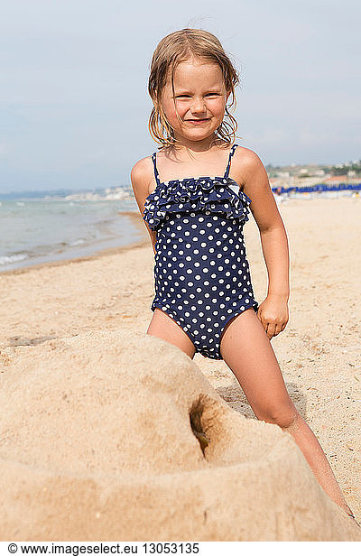 Cute girl building sandcastle on beach in spotted swimming costume  portrait  Castellammare del Golfo  Sicily  Italy