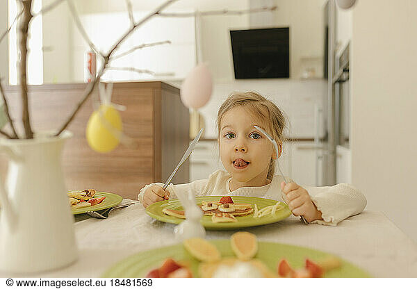 Cute girl eating pancakes for breakfast at home