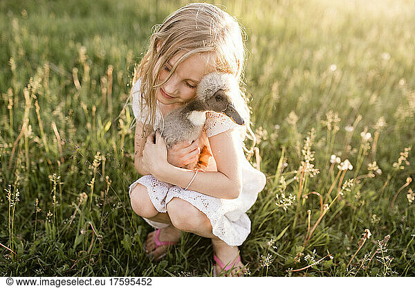 Cute girl embracing baby duck in meadow