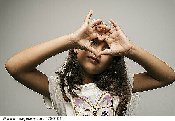 Cute girl gesturing heart shape against gray background
