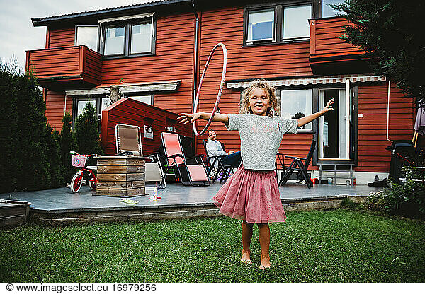 Cute girl in tutu playing with hula hoop in her backyard in Norway