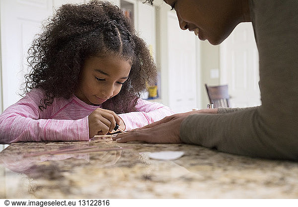 Cute girl painting mother's fingernails at home