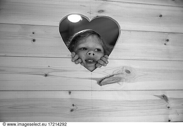 Cute girl peering through heart shape in wood
