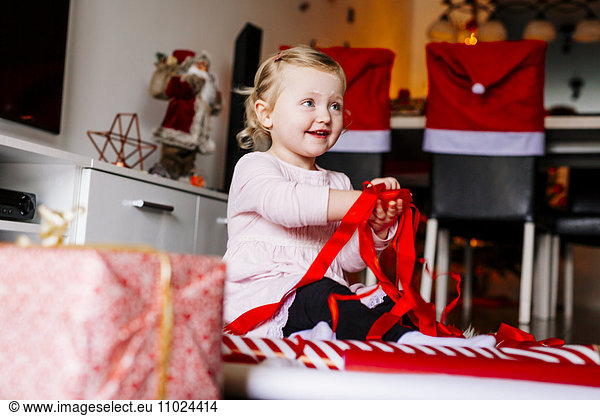 Cute girl playing with red ribbons while wrapping Christmas presents y