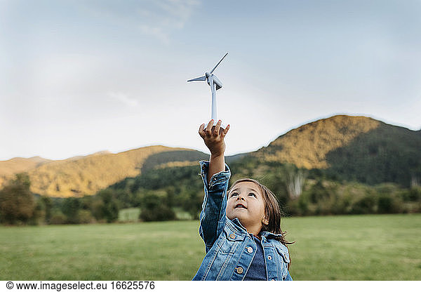 Cute girl playing with wind turbine toy while standing at backyard
