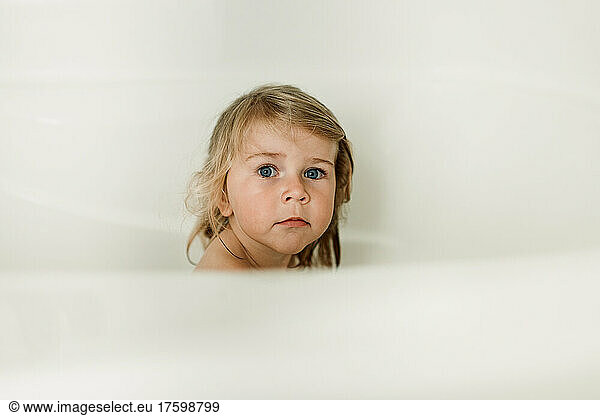 Cute girl sitting in bathtub by white wall