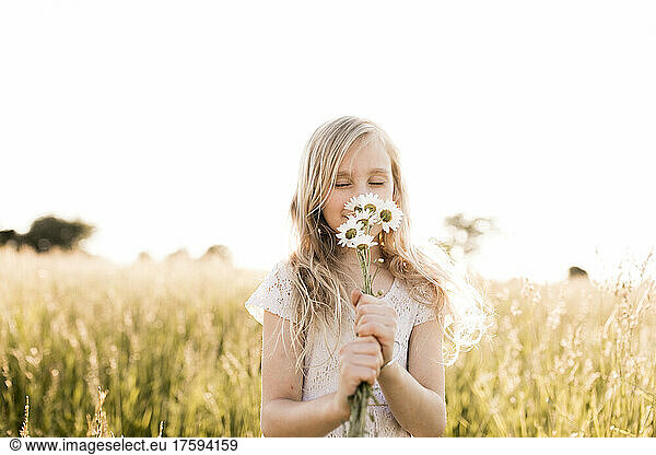 Cute girl smelling daisy flowers in field