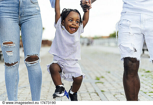 Cute girl swinging while holding hands of parents