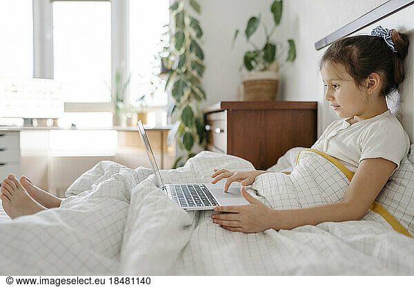 Cute girl using laptop on bed in bedroom