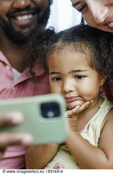 Cute girl watching smart phone with parents at home