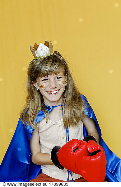 Cute girl wearing crown and boxing gloves against yellow background