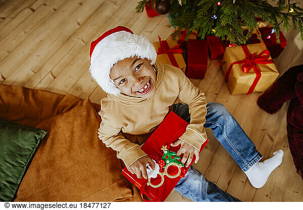 Cute girl wearing Santa hat opening gifts iunder Christmas tree at home