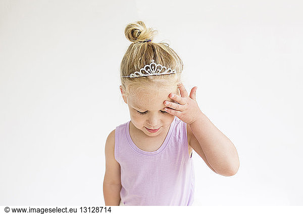 Cute girl wearing tiara touching forehead while standing against white background